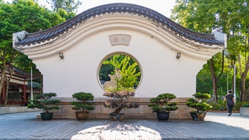 A moon gate with a curved roof near the entrance frames the view of the lush landscape in the park.